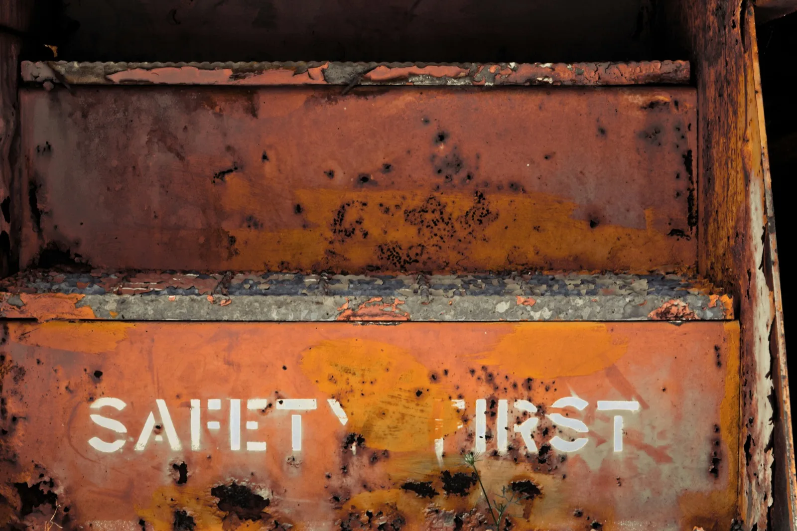 Weathered orange metal surface stenciled with the words SAFETY FIRST